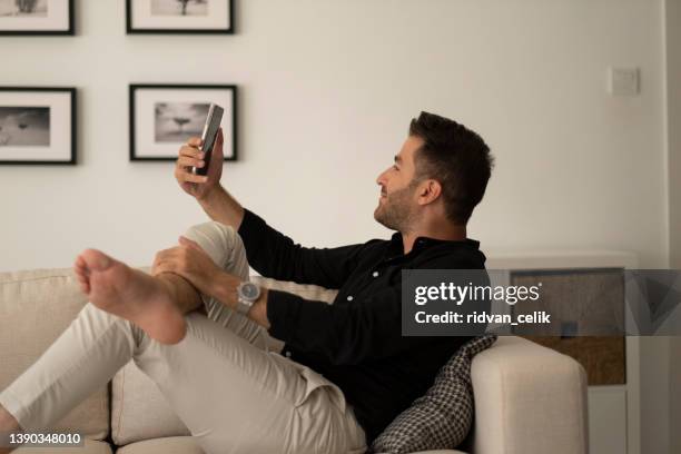 young man sitting on sofa holding smartphone communicating - human body part videos stock pictures, royalty-free photos & images