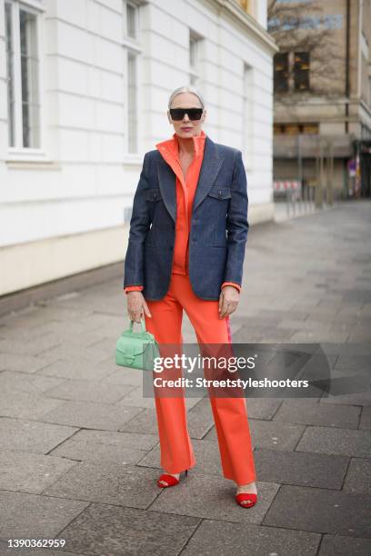 Best ager model and influencer Petra van Bremen wearing a dark blue denim jeans blazer by Saint Laurent, an orange jacket and matching pants by...