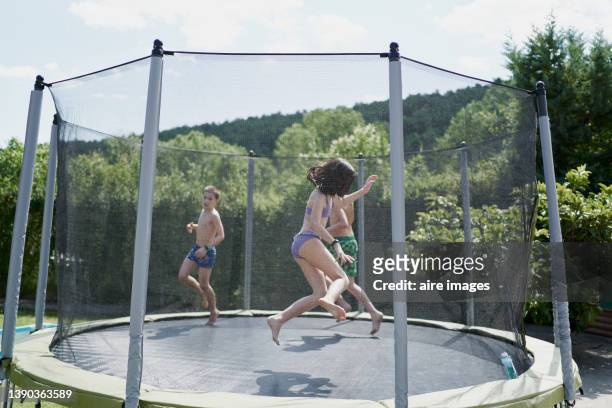 children jumping on a trampoline placed in the backyard of the house on a sunny day - netting stock pictures, royalty-free photos & images