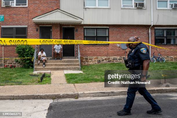 Baltimore Police officer walks past residents the site of a mass shooting in the Brooklyn Homes neighborhood on July 2, 2023 in Baltimore, Maryland....