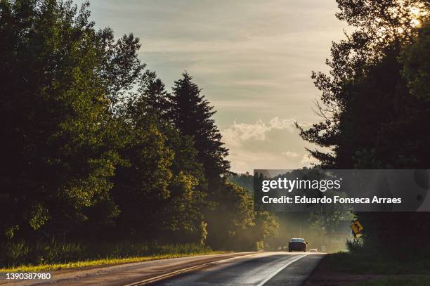 sunset shining on cars driving on a wet back road after the rain - cars on a road sunny photos et images de collection