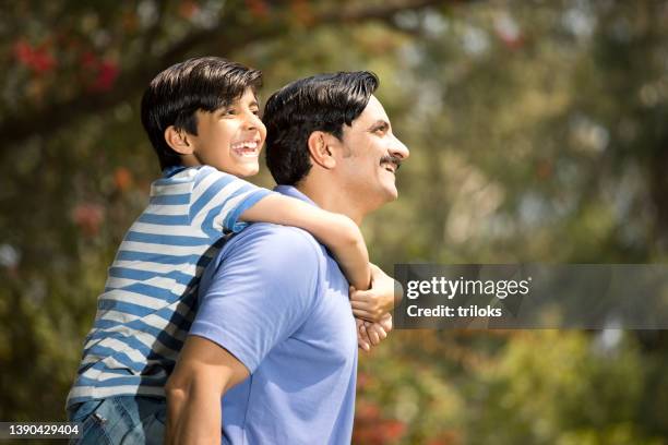 father and son admiring view at park while giving piggyback ride to son - father son admiration stock pictures, royalty-free photos & images