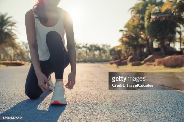running shoes. woman tying shoe laces. closeup of female sport fitness runner getting ready for jogging outdoors on forest path in late summer or fall. jogging girl exercise motivation heatlh and fitness. - joggerin park stock-fotos und bilder