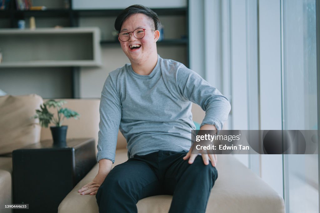 Porträt Asiatisches chinesisches Down-Syndrom junger Mann schaut lächelnd in die Kamera im Wohnzimmer