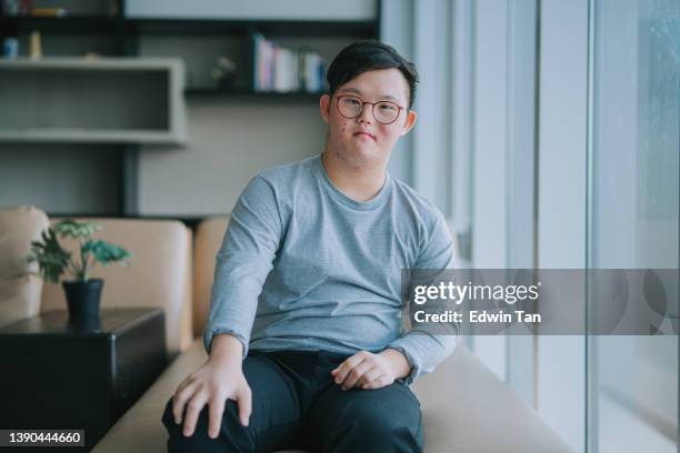 portrait asian chinese down syndrome young man looking at camera smiling in living room - mental disability stock pictures, royalty-free photos & images