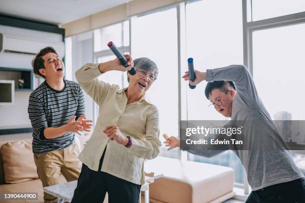 multi generation asian chinese down syndrome young man singing dancing with grandmother and father having fun in living room during weekend - grandmas living room stockfoto's en -beelden