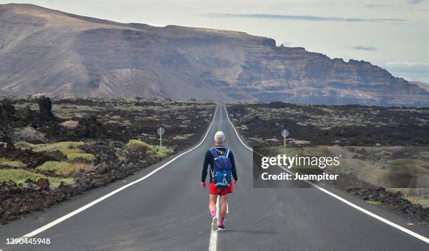 lonely oung man walking  on an endless road in a volcanic landscape in lanzarote, canary islands - 長 ストックフォトと画像