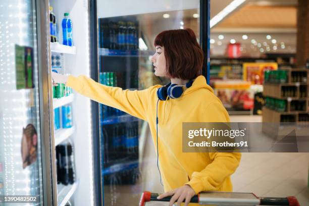 side view of a young caucasian woman doing her shopping in supermarket - koude dranken stockfoto's en -beelden