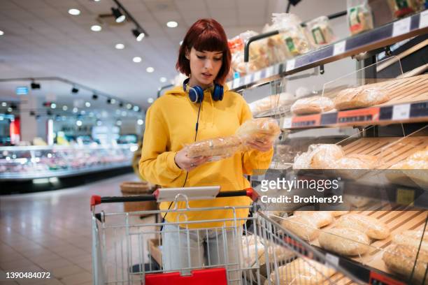 junge kaukasische frau, die ihre einkäufe im supermarkt erledigt - supermarket bread stock-fotos und bilder