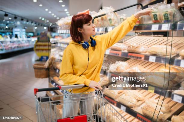 junge kaukasische frau, die ihre einkäufe im supermarkt erledigt - supermarket bread stock-fotos und bilder