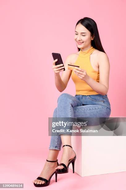 portrait of cheerful businesswoman holding mobile phone and credit card while sitting against pink background - phone credit card stock-fotos und bilder