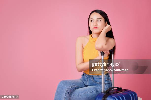 young woman with suitcase sitting bored against pink background - airport frustration stock pictures, royalty-free photos & images