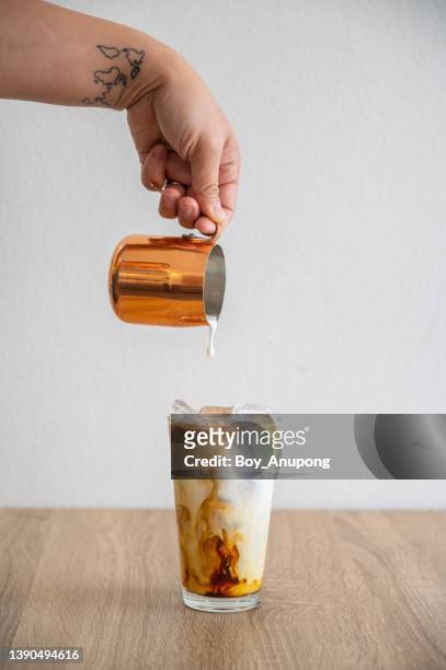 barista hand pouring milk into an iced coffee for making iced latte. - coffee and milk stock pictures, royalty-free photos & images