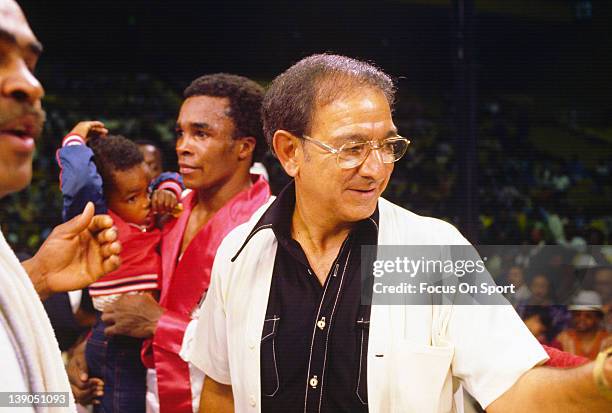 Boxing trainer Angelo Dundee, right, looks on after a welterweight fight involving Sugar Ray Leonard, left, holding his young son Ray Jr. Circa 1977.