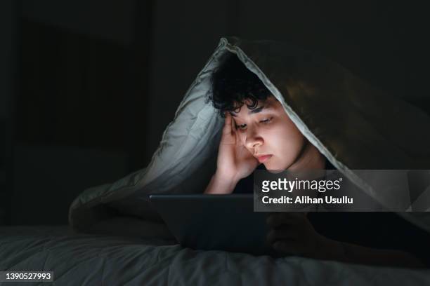 悲しそうな表情で深夜にベッドでスマホを使う10代の少女 - media night ストックフォトと画像