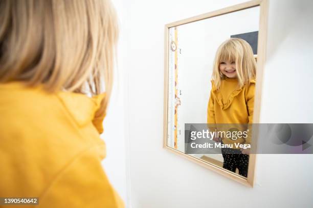 rear view of little girl contemplating her reflection in the mirror with playful attitude. - girl hair stock pictures, royalty-free photos & images