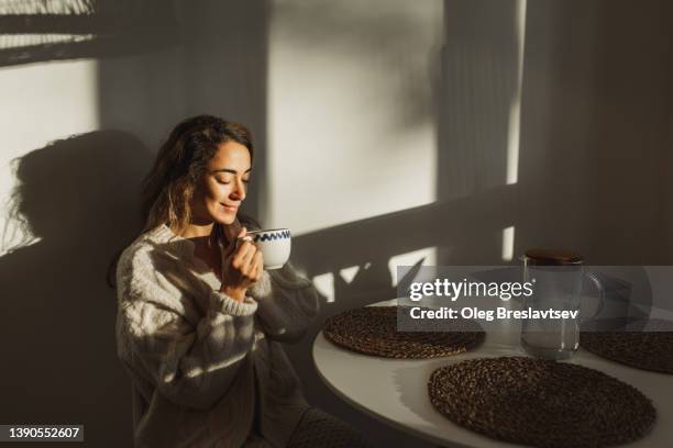 young pretty woman enjoying morning coffee at home. beautiful sun light in kitchen room. - matin photos et images de collection