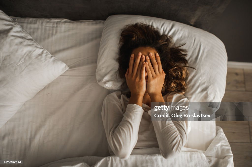Woman in depression closed face with hands and crying in bed. Melancholy mood, mental health. Life problems