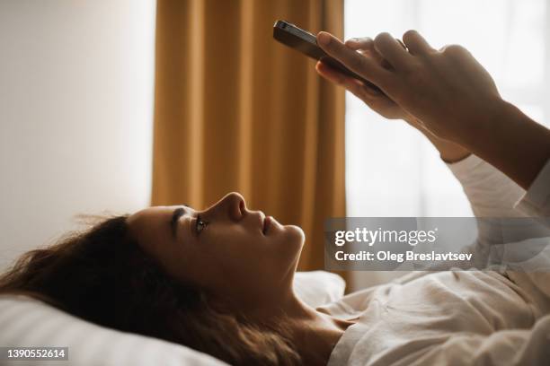 internet and gadget addiction. wasting time in smartphone. woman lying in bed with phone - woman brown hair stock pictures, royalty-free photos & images