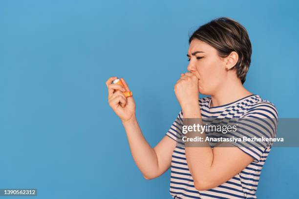 coughing girl holding an inhalation can in her hand against blue backgrounds - woman cough stock-fotos und bilder