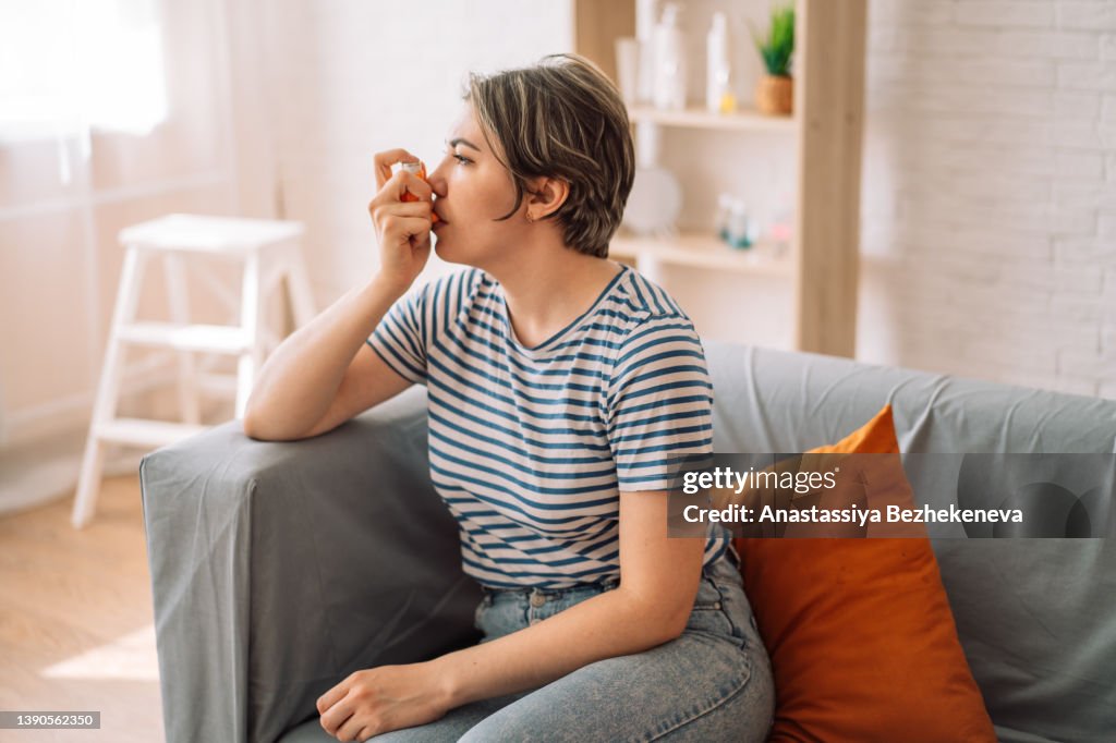 Woman sits on couch and inhales medicine from an inhalation can
