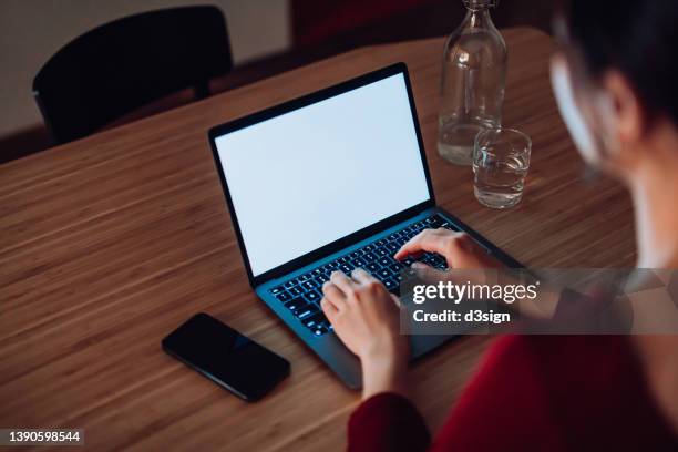 over the shoulder view of young asian woman using laptop at home in the evening. cropped shot of female typing on computer keyboard, working late. laptop with blank screen for design mockup. lifestyle and technology - mockup identity photos et images de collection