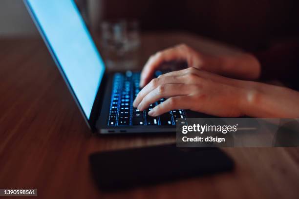 close up of female hands typing on computer keyboard while sitting on desk in the evening, with smartphone by the side. close up of woman's hand using laptop at home. technology in everyday life - financial crime stock pictures, royalty-free photos & images