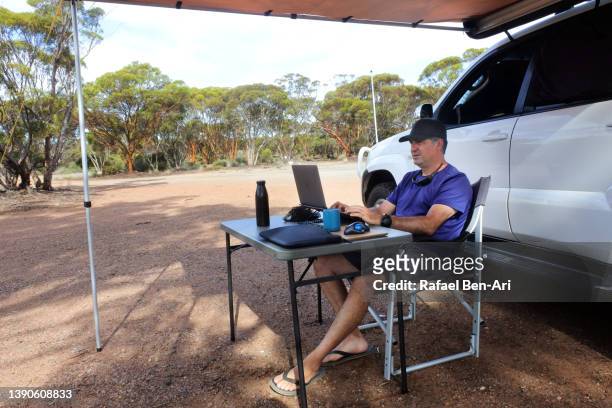 australian man working on a laptop outdoors beside his vehicle during a road trip - four wheel drive australia stock pictures, royalty-free photos & images