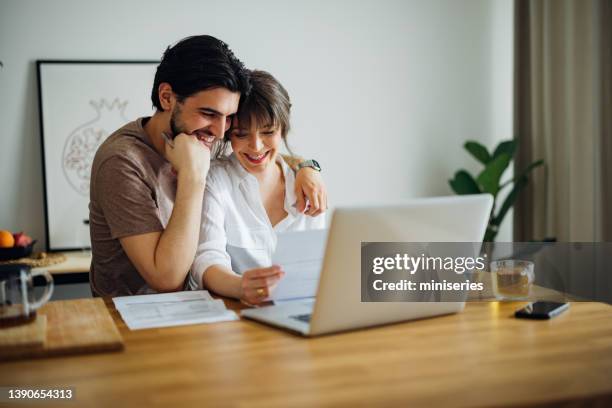 smiling couple paying bills at home - hoog stockfoto's en -beelden