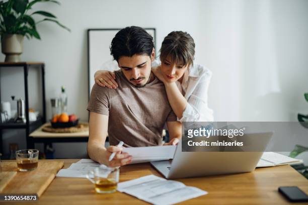 smiling couple paying bills at home - rekening stockfoto's en -beelden