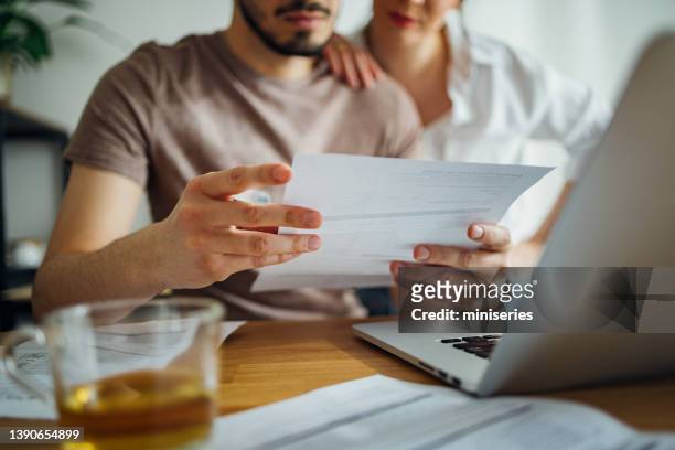 unrecognizable couple paying bills at home - man holding paper stock pictures, royalty-free photos & images