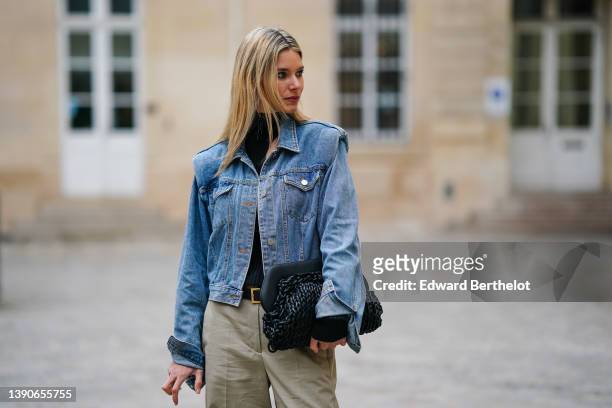Natalia Verza @mascarada.paris wears a black turtleneck / cut-out asymmetric shoulder / long sleeves body, a blue denim oversized jacket, a black...