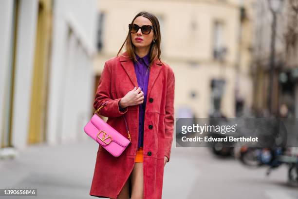 Maria Rosaria Rizzo @lacoquetteitalienne wears white pearl pendant earrings, a purple shirt, a neon orange short skirt, a red velvet long coat, a...