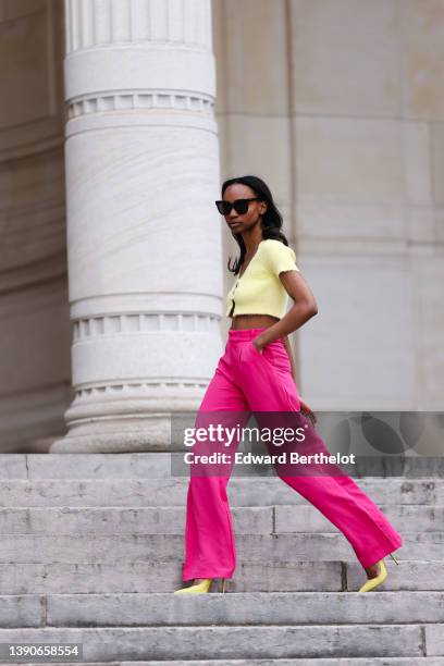 Emilie Joseph @in_fashionwetrust wears black sunglasses, silver rhinestone earrings, a pale yellow wool / buttoned / cropped t-shirt, high waist neon...