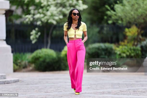 Emilie Joseph @in_fashionwetrust wears black sunglasses, silver rhinestone earrings, a pale yellow wool / buttoned / cropped t-shirt, high waist neon...