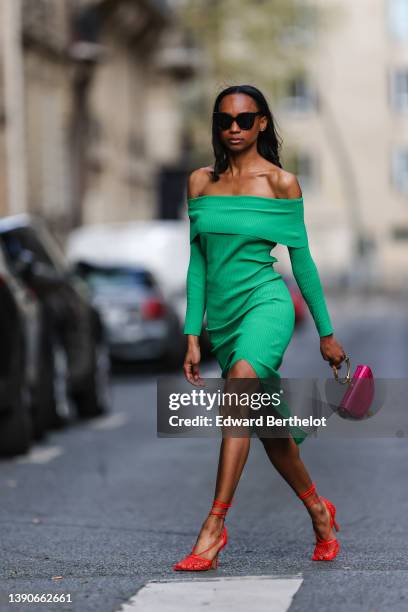 Emilie Joseph @in_fashionwetrust wears black sunglasses, rhinestone earrings, a green ribbed wool high neck / slit tube midi dress, a pink shiny...