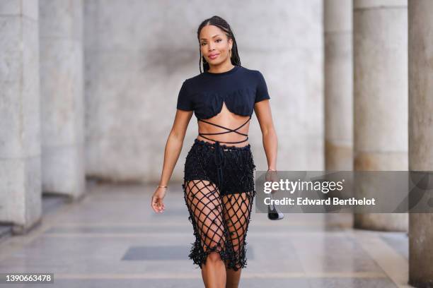 Ellie Delphine wears gold earrings, a black cropped / heart neck / laces waist t-shirt, a black pearls mesh / checkered tube knees skirt, black...