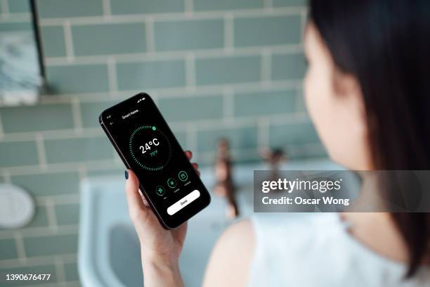 over the shoulder view of young woman adjusting room temperature via smart home app on smart phone. - control room monitors stockfoto's en -beelden