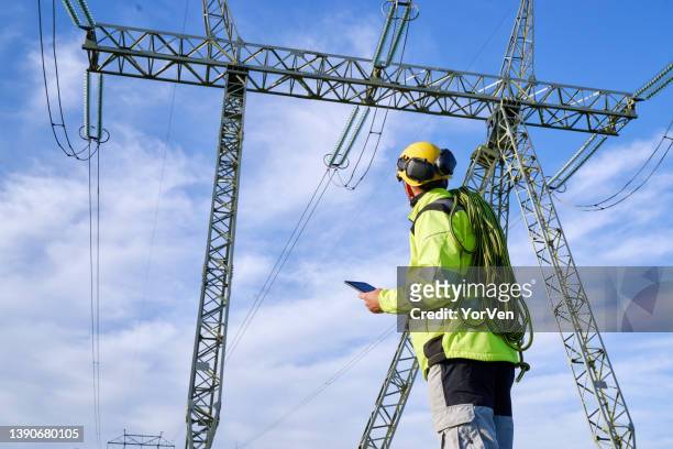 ingeniero eléctrico mirando hacia arriba en la torre de alto voltaje - alto voltaje fotografías e imágenes de stock