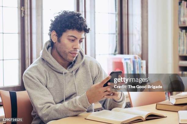 young man looking at smart phone while studying in library - students college beautiful bildbanksfoton och bilder