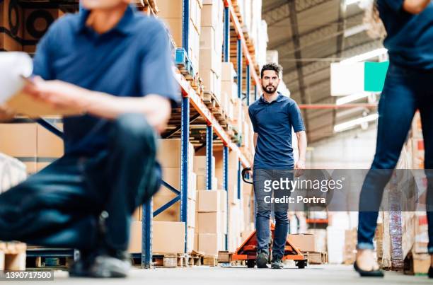 warehouse worker pulling pallet jack with packages - pallet jack stock pictures, royalty-free photos & images