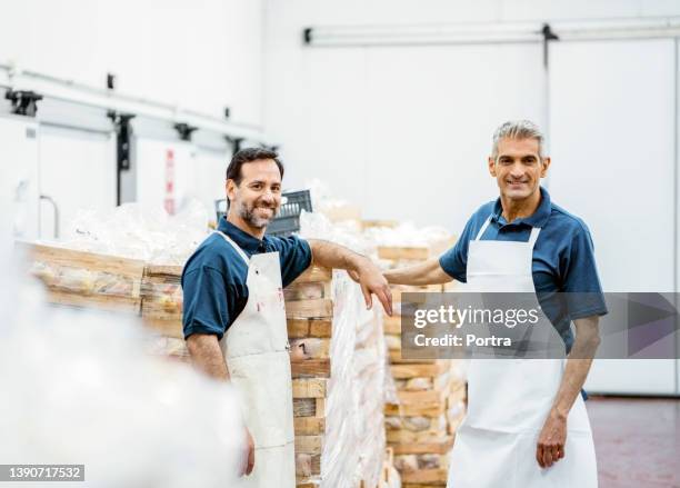 porträt von zwei glücklichen metzgern, die im fleischverpackungslager arbeiten - metzgerei stock-fotos und bilder