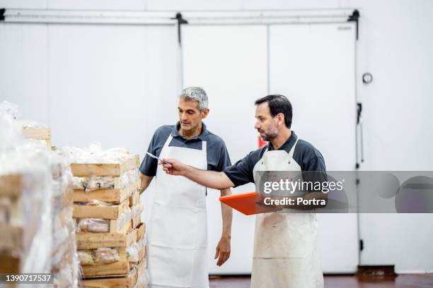 two workers taking inventory of packaged meat wooden boxes in warehouse - koelkast stockfoto's en -beelden