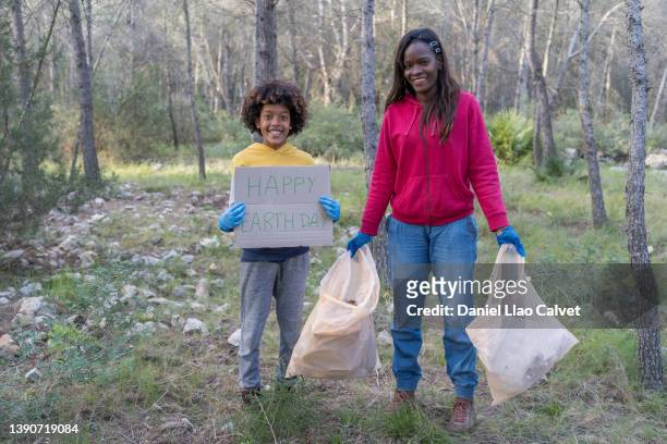 boy holds up a "happy earth day" sign with his mother - happy earth day stock-fotos und bilder