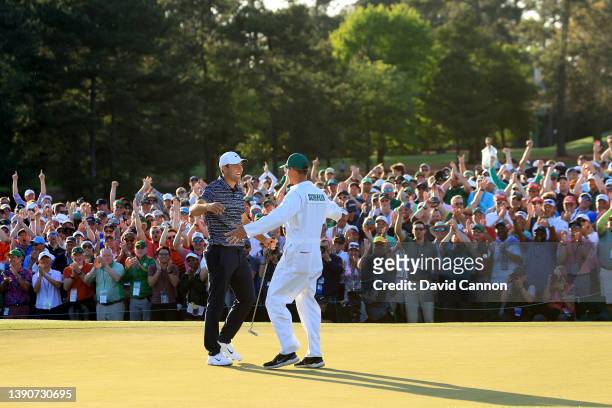 Scottie Scheffler and caddie Ted Scott embrace on the 18th green after winning the Masters at Augusta National Golf Club on April 10, 2022 in...
