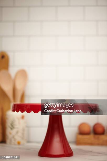 bright white modern kitchen with tile backdrop and marble countertop with empty red cake stand for product display - cakestand stock-fotos und bilder