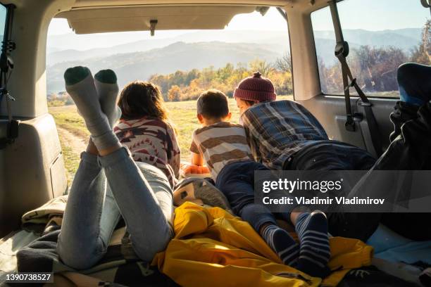 um jovem casal e seu filho estão se divertindo descansando na parte de trás de sua van campista e olhando para a paisagem - family inside car - fotografias e filmes do acervo