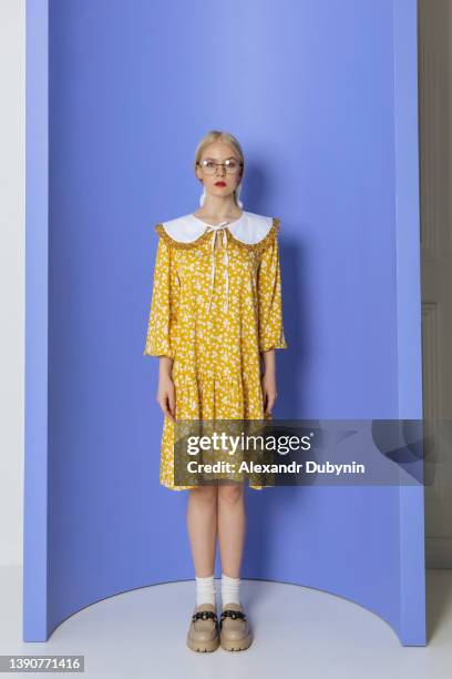 young beautiful woman in yellow dress looking at camera on blue background indoors. girl model in glasses posing in a new collection of summer clothes studio shot - 襟 ストックフォトと画像