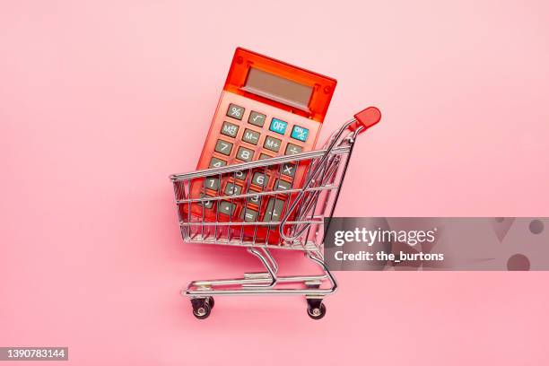 still life of red calculator in a small shopping cart on pink background - inflation stock-fotos und bilder