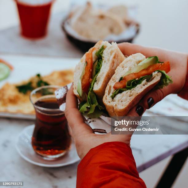 sándwich de desayuno por la mañana, té negro (té turco), tomate de pepino y sándwich de verduras, persona que come sándwich, sándwich de mano humana, persona que come en el café - bocadillo de beicon lechuga y tomate fotografías e imágenes de stock